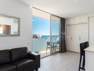 Spacious living room with large windows, light wood floors, and minimalist decor. Natural lighting highlights soft textures and neutral colors.