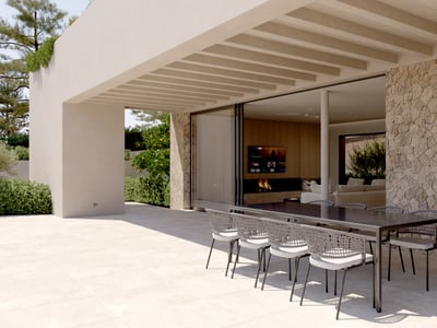 A modern covered terrace with a large black dining table, woven chairs, natural stone wall, and sliding glass doors.