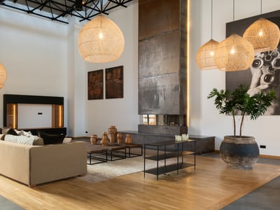 Großzügiges Wohnzimmer mit hohen Decken, großem Metallkamin, Korbpendelleuchten und modernem beigen Sofa.