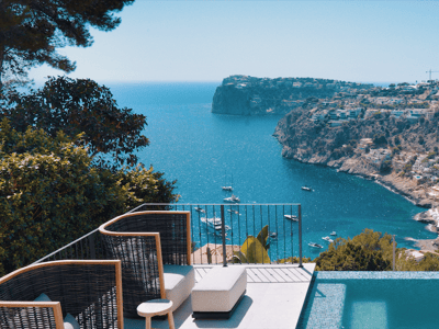 Luxury terrace featuring an infinity pool and designer lounge chairs overlooking a bay with yachts and cliffs.