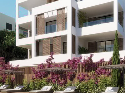 Vit modern lägenhetsbyggnad med fönsterluckor i trä, glasbalkonger och rosa bougainvillea vid ett poolområde.