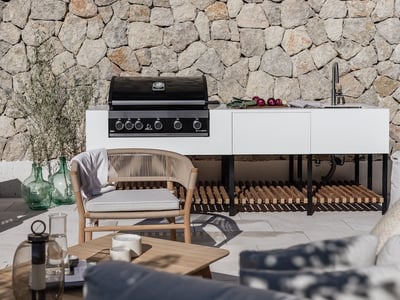 Moderne weiße Außenküche mit Gasgrill und Spüle vor einer Natursteinwand mit Designer-Terrassenmöbeln.