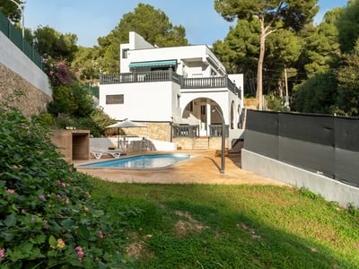 Villa blanca con piscina privada, zona de terraza, césped y rodeada de un frondoso bosque de pinos.