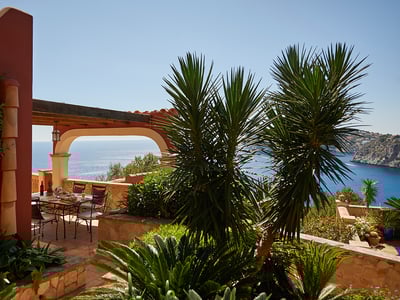 Comedor exterior en una terraza de terracota con pérgola de arco y vistas panorámicas al mar azul.