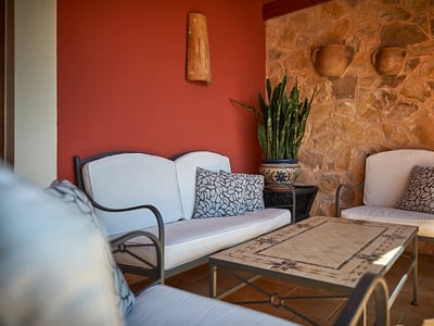 Terraza con sofás blancos, mesa de mosaico, pared de piedra natural y una pared de acento roja.
