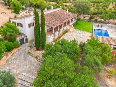 Vista desde arriba de una villa con tejado de terracota, patio de piedra, piscina azul y jardines frondosos.