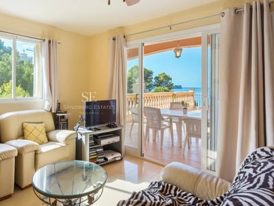 Interior luminoso con ventanales grandes, suelo de madera clara, y mobiliario moderno. Vistas panorámicas al mar.