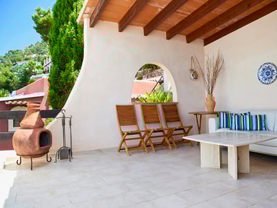 Terraza cubierta con sofás blancos, mesa de mármol, chimenea de barro y vigas de madera a la vista.
