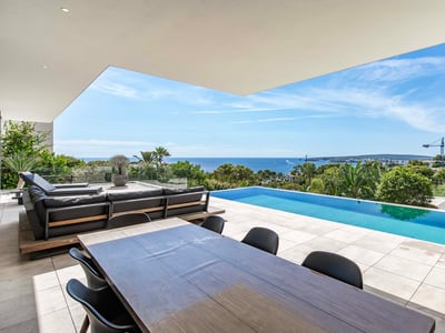 Terraza de lujo moderna con piscina infinity frente al mar, zona de comedor exterior y sofás.