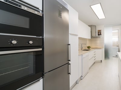 Una cocina moderna de estilo galería con armarios blancos y electrodomésticos de acero inoxidable.