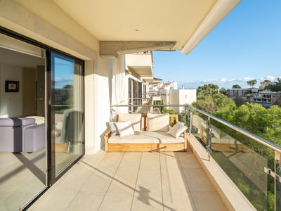 Modern balkong med träsoffa och glasräcke med utsikt över en frodig tallskog under en klarblå himmel.