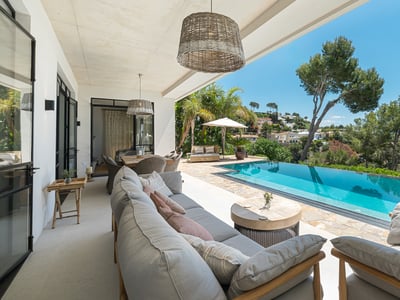 Terraza cubierta con sofás grises frente a una piscina infinita turquesa y el mar Mediterráneo.