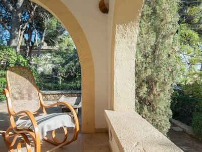 Una mecedora clásica de madera en una terraza con arcos de piedra y vistas a un jardín frondoso.