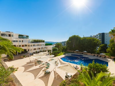 Großer blauer Swimmingpool umgeben von einer beigen Terrasse, weißen Sonnensegeln und Palmen unter hellem Sonnenschein.