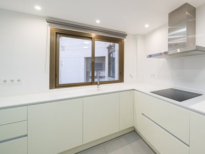 Cocina minimalista blanca con encimera en L, placa de inducción, campana de acero inoxidable y ventana.