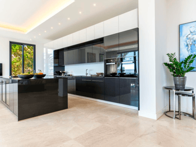 Amplia cocina moderna con isla negra brillante, armarios oscuros y suelo de piedra clara bajo luz natural.