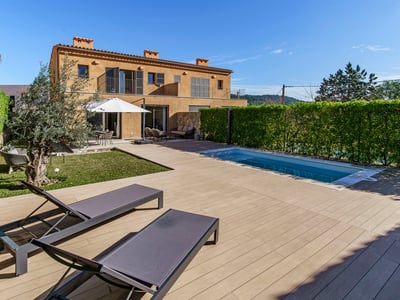 Modern outdoor pool and wooden deck with sun loungers next to a terracotta villa under a clear blue sky.