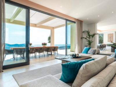 Amplio salón moderno con sofá beige, ventanales de suelo a techo y terraza con vistas al mar.