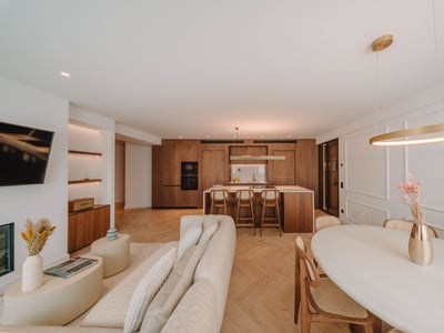 Rymligt lyxigt vardagsrum med beige soffa, fiskbensparkett och integrerat kök i naturträ.