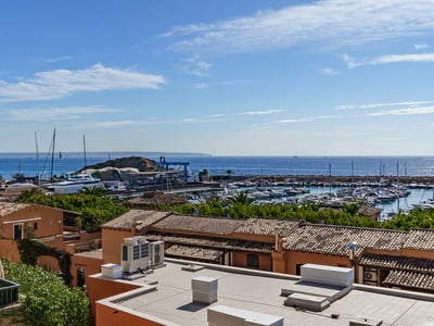 Vue surélevée d'une marina méditerranéenne avec des toits en terre cuite, des yachts blancs et la mer bleue.