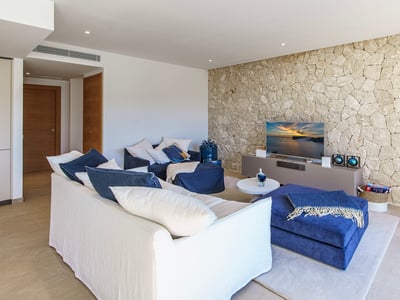 Contemporary living room featuring a white sofa, navy blue ottomans, and a textured natural stone wall with a TV.