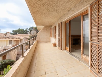 Long tiled balcony with weathered wooden shutters and glass doors leading to an indoor living area.
