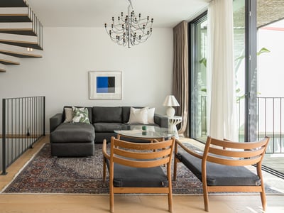 Contemporary living room featuring a gray sectional, wooden spiral stairs, and floor-to-ceiling windows.