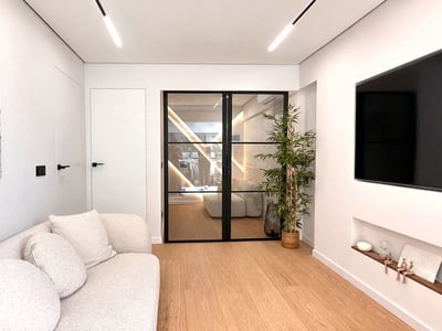 Modern living room featuring a white textured sofa, light wood floors, and black-framed glass double doors.