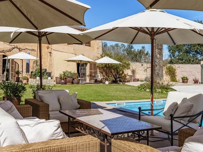 A luxury swimming pool surrounded by large white umbrellas and wicker lounge furniture in a Mediterranean garden.