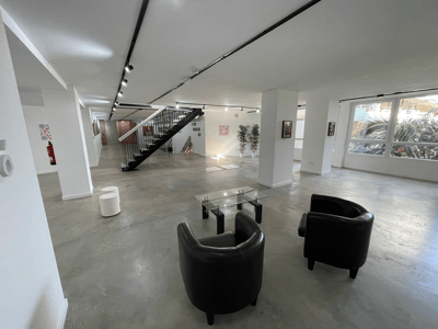 Amplio espacio con suelos de hormigón pulido, sillones de cuero negro y una escalera metálica minimalista.