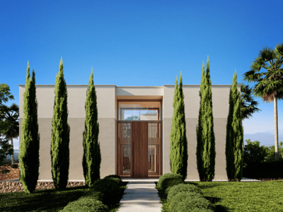 Entrada simétrica de villa moderna con cipreses altos, puerta de madera y cielo azul despejado.