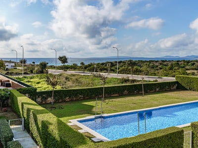 Rektangulär blå pool omgiven av gräsmatta och häckar med Medelhavet i bakgrunden under en molnig himmel.