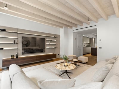 Salón moderno con sofás blancos, mesa de mármol, techo de vigas de madera y mueble de TV integrado.