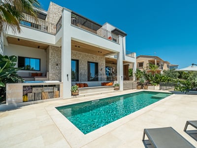 Außenansicht einer modernen Villa mit Pool, gepflegtem Rasen und großen Fenstern, die das Sonnenlicht reflektieren.