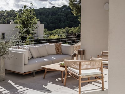 Moderner Sitzbereich auf einer Terrasse mit weißem Sofa, Holzstühlen und Blick auf einen üppigen grünen Wald.