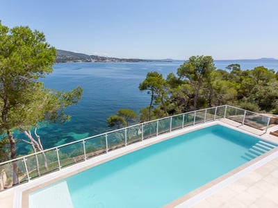 Rechteckiger türkisfarbener Pool mit Blick auf das Mittelmeer, umgeben von Kiefern und Glasgeländer.