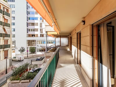 Lång solig balkong med orange markis och metallräcke med utsikt över en stadsgata.