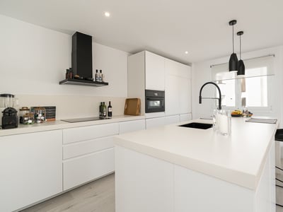 Modern white kitchen with a large island, black faucet, and sleek integrated appliances.