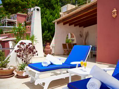 Terraza soleada con tumbonas de color azul vibrante, toallas blancas y un porche con vigas de madera.