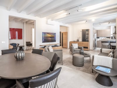 Salón de planta abierta con mesa de comedor redonda, sofás de cuero y techo con vigas blancas.