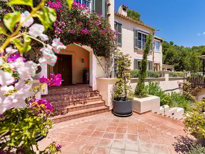 Terrakottatrappa som leder till en trädörr på en villa inramad av rosa bougainvilleablommor.