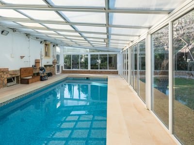 Piscina interior con mosaicos azules, paredes de piedra y techo translúcido junto a grandes ventanales.