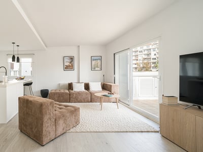 Bright modern living room with a brown corduroy modular sofa, textured rug, and a minimalist white kitchen.