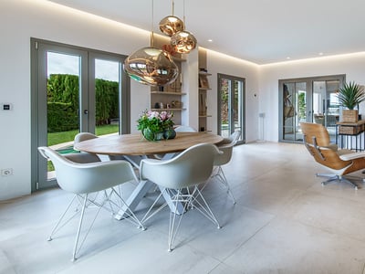 Salón moderno con comedor, sillas de diseño, lámparas de cobre y sofá gris con acceso al jardín.