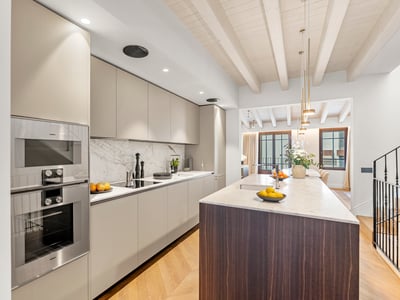 Cocina moderna con gabinetes beige, encimera de mármol blanco, isla de madera oscura y techo de vigas de madera clara.