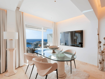 Ein modernes Esszimmer mit einem Glastisch, Designstühlen und großen Fenstern mit Blick auf das Mittelmeer.