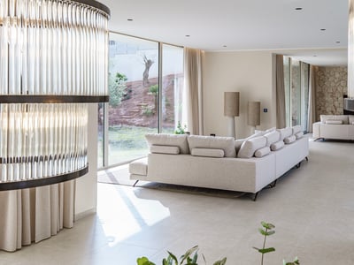 Amplio salón moderno con sofá crema, grandes ventanales al jardín y pared de piedra natural al fondo.