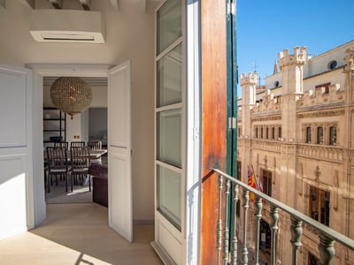 Blick von einer offenen Balkontür auf ein historisches gotisches Steingebäude unter klarem blauem Himmel.