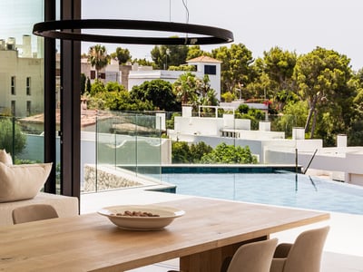 Helles Esszimmer mit Holztisch und Blick auf einen Pool und grüne Landschaft durch große Glasfronten.