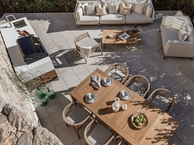 Draufsicht auf eine Steinterrasse mit Teakholz-Essgruppe, weißen Sofas und einer modernen Außenküche.